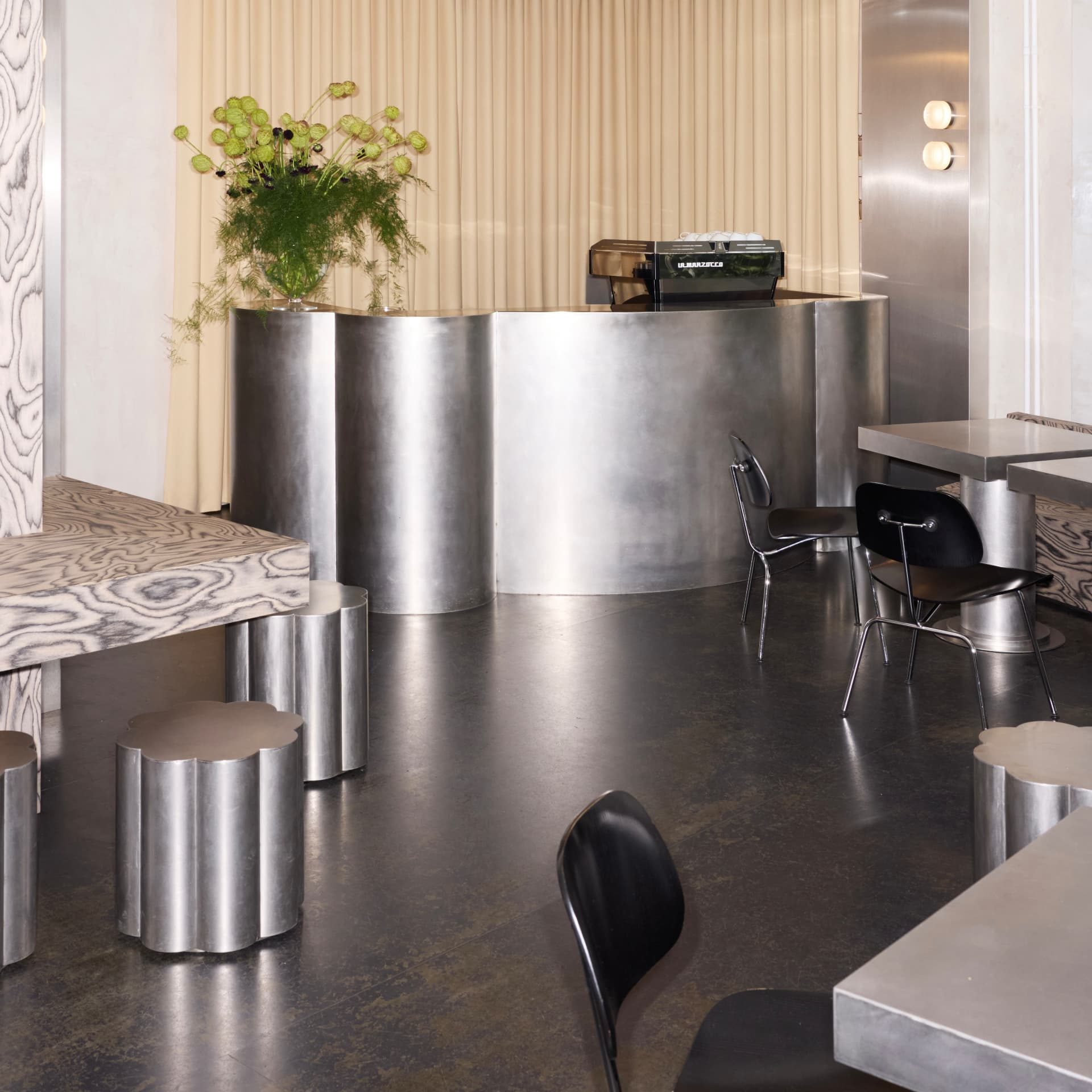 Interior of DRAFT. Zürich showing the curved steel counter, cloud-shaped metal stools and black bentwood chairs